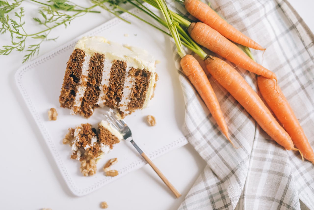 A slice of carrot cake with cream cheese frosting and fresh carrots beautifully arranged.